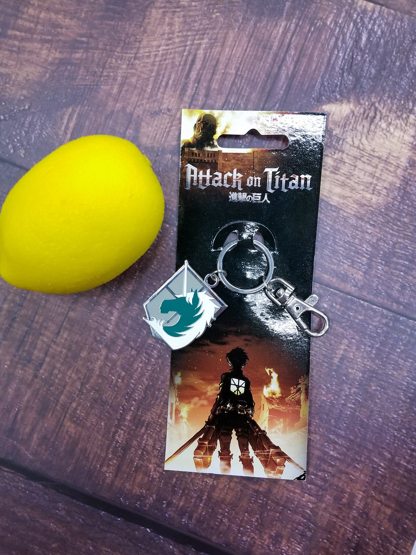 An enameled metal keychain with clip and ring, depicting the Military Police Brigade emblem from Attack on Titan.  The metal emblem is approximately 1 inch wide by 1.5 inches tall.