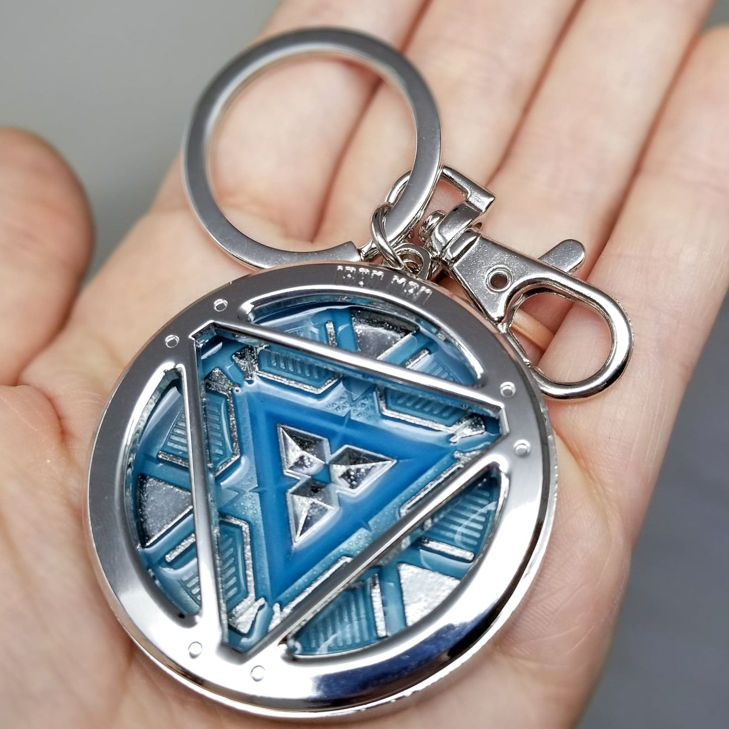 Iron Man Glow-In-The-Dark Pewter Arc Reactor Keychain.  In Celebration of Tony Stark’s Iron Man as seen in the Marvel Studios Avengers films, this oversize pewter Arc Reactor glow-in-the-dark metal keychain features the Arc Reactor powering Tony’s chest and power suit in Iron Man 3.  2 inches across & nearly 1/2 inch thick!  Features “Iron Man” logo on the back Includes stainless steel keyring and clip Blue Glow-in-the-Dark effect!  Carry your own Proof that Tony Stark Has a Heart