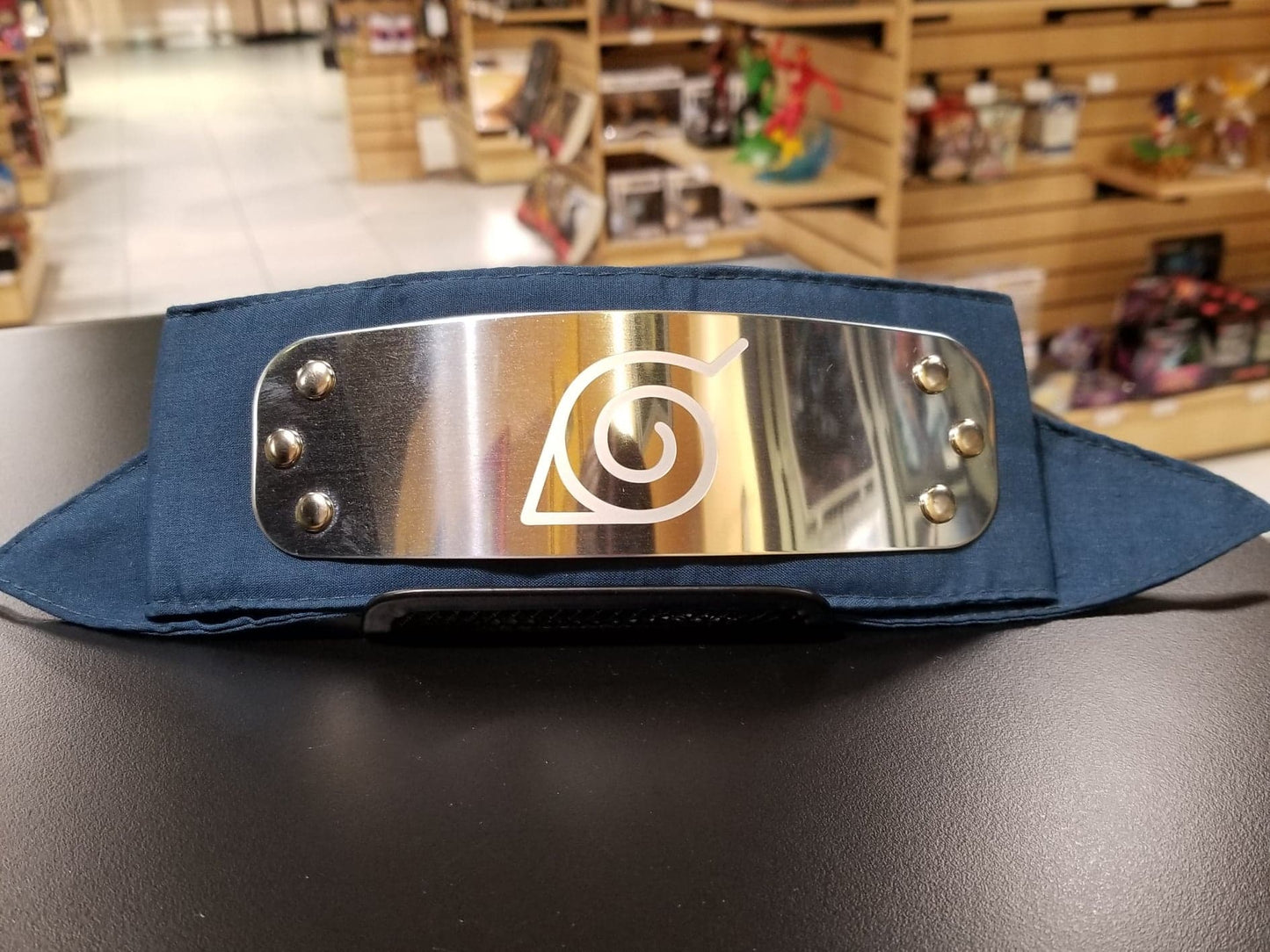Load image into Gallery viewer, In the beloved anime Naruto, a forehead protector is a headband composed of a metal plate and a band of cloth. These iconic headbands are worn by most shinobi and are engraved with the symbol of their hidden village. Leaf Village is Naruto&amp;#39;s village.   This fully licensed forehead protector replica features a sturdy metal plate with a stunning reflective shine, a laser engraved Hidden Village symbol, and long fabric ties. The headband is made in one-size, designed to fit the average adult. 
