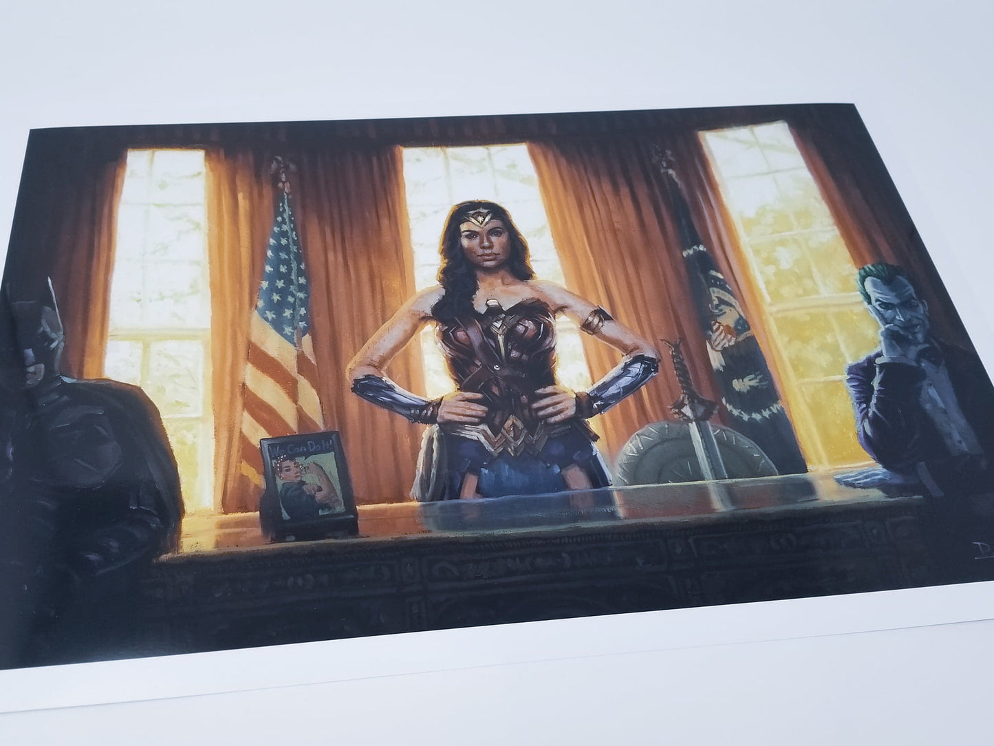 Load image into Gallery viewer, Wonder Woman in the Oval Office Art Print By Bucket Art  What if Diana Prince were Madam President of the USA? Wonder Woman stands at the Resolute Desk in the Oval Office, continuing to fight for truth, love, and justice.  Wonder Woman wears her iconic armor. Batman and The Joker are seated on each side of her desk symbolizing bipartisanship. Look for the &amp;quot;We Can Do It&amp;quot; framed image on her desk. Wonder Woman’s shield and the Godkiller sword are behind her.
