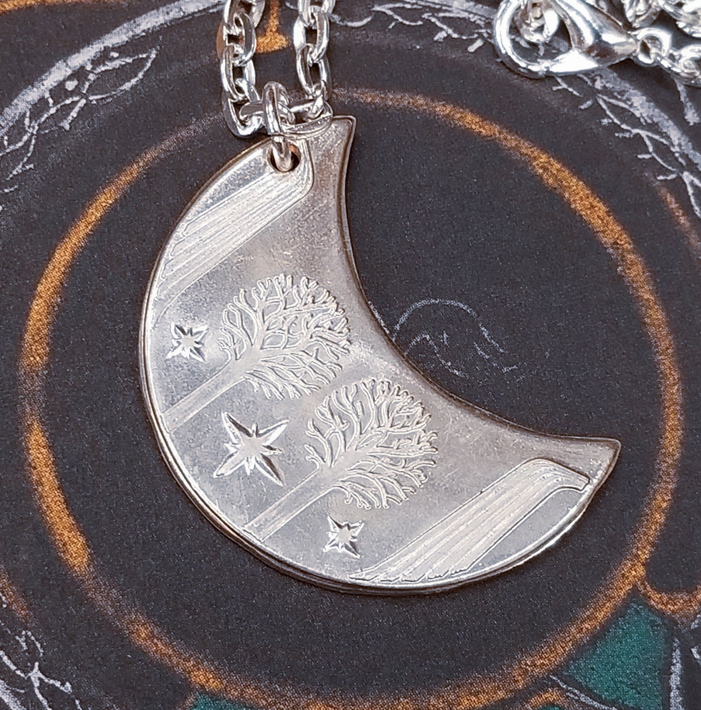 Elvish coin from Rivendell is shaped like a crescent moon. It depicts the valley containing the ancient trees of silver and gold and the three Silmarils, represented as stars. The text in Tengwar translates from Sindarin to Elrond Peredhil, Lord of Rivendell, The Last Homely House East of the Sea. It includes the date that Thorin and Company meet Elrond at Rivendell before continuing on to The Lonely Mountain.  This Rivendell Moon is crafted in celebration of The Lord of the Rings by J. R. R. Tolkien